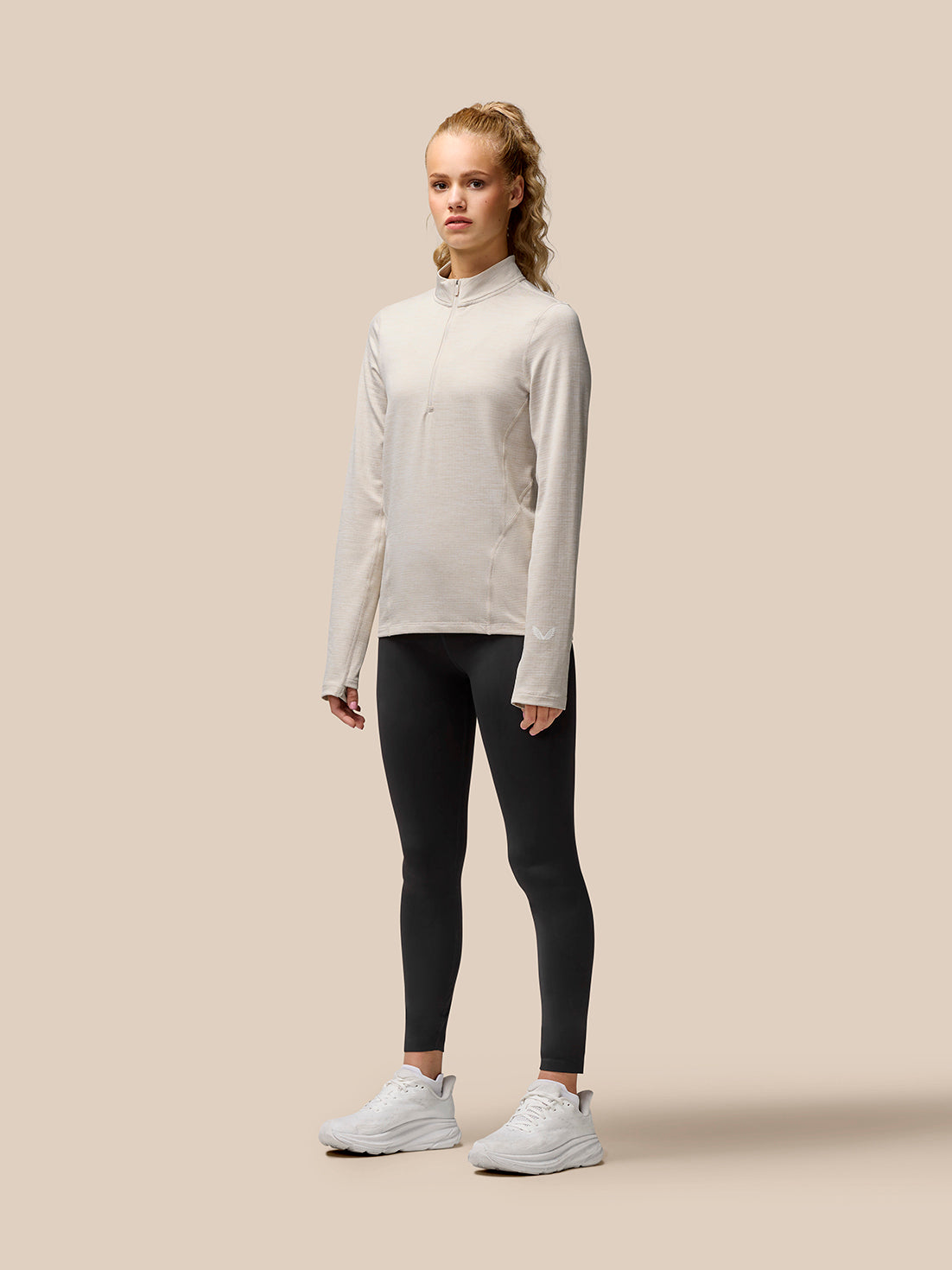 Model wearing Flow Training Beige half zip top with funnel collar and long sleeves, paired with black leggings.