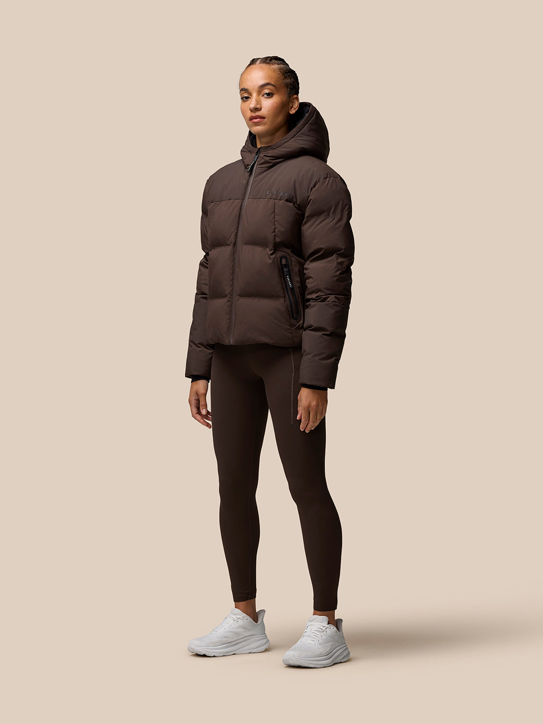 Full body shot of a woman wearing a brown Quilts Lifestyle Jacket with hood, zip front and pockets.