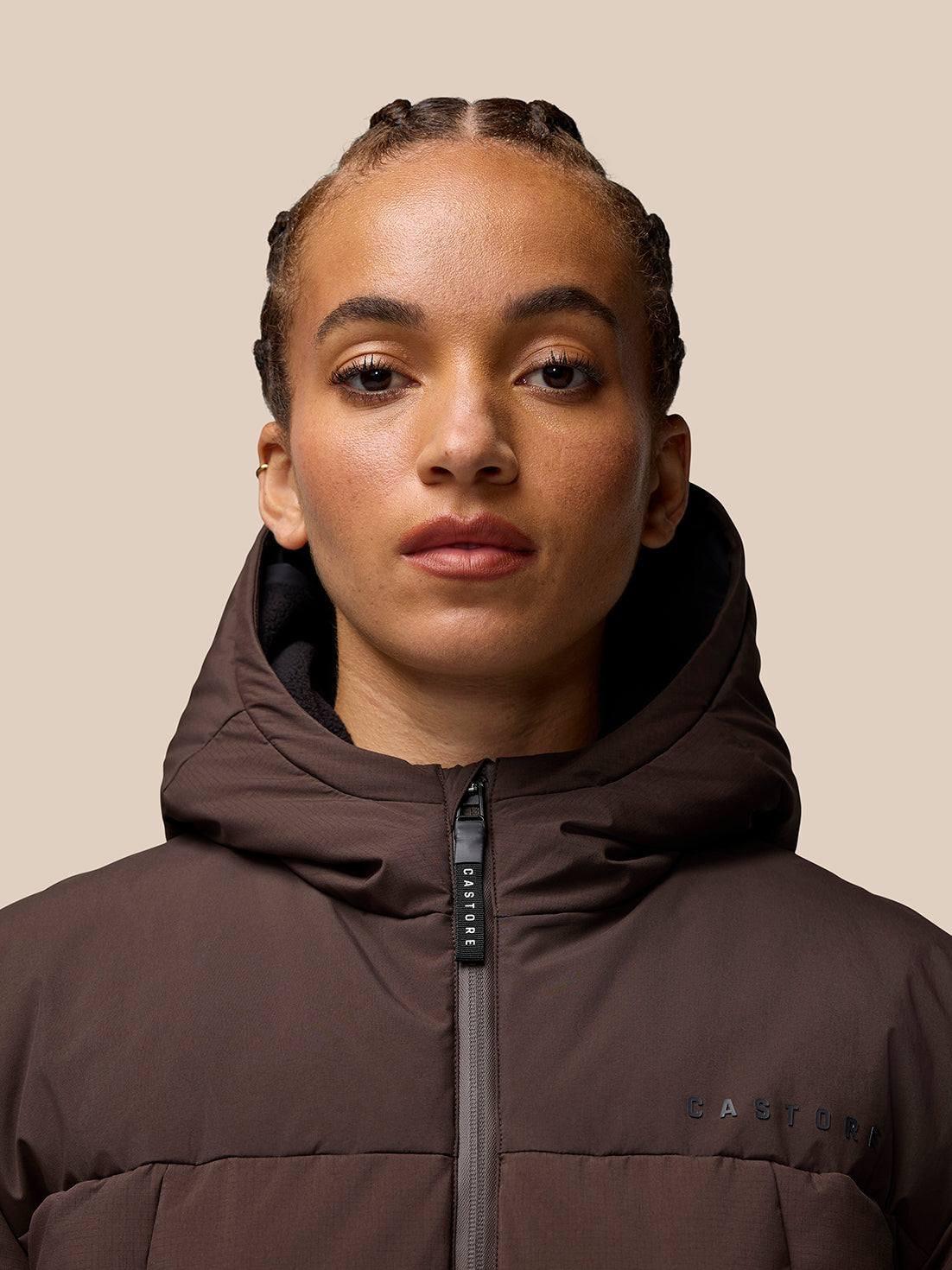 Close-up of a model wearing the brown Quilts Lifestyle Jacket with hood up and Castore branding on the chest.
