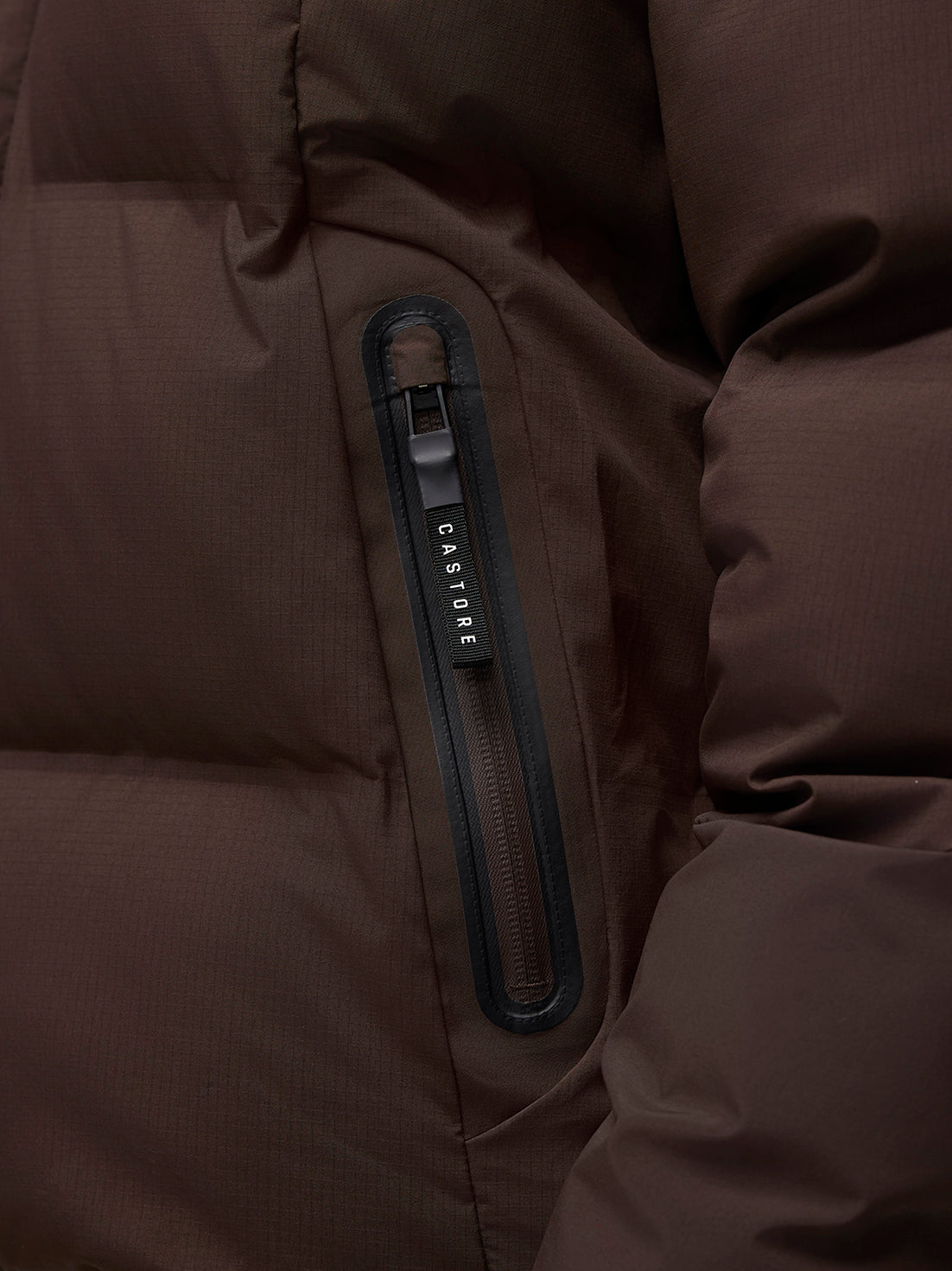 Close-up of the brown Quilts Lifestyle Jacket pocket with vertical zipper and Castore branding.