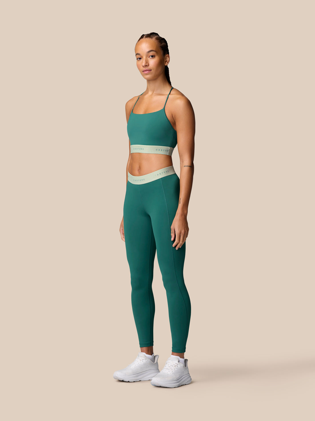 Full-body shot of a model wearing seafoam Adapt Training Leggings with a matching top and white sneakers against a beige backdrop.