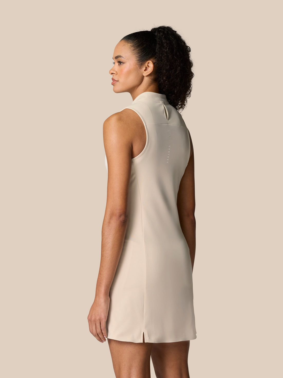 Model wearing Pinnacle Dress Stone shown from the back, highlighting a streamlined sleeveless silhouette and split hem.