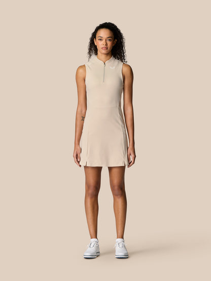 Pinnacle Dress in Stone worn by a model; sleeveless beige athletic dress with a zip neckline and split hem.