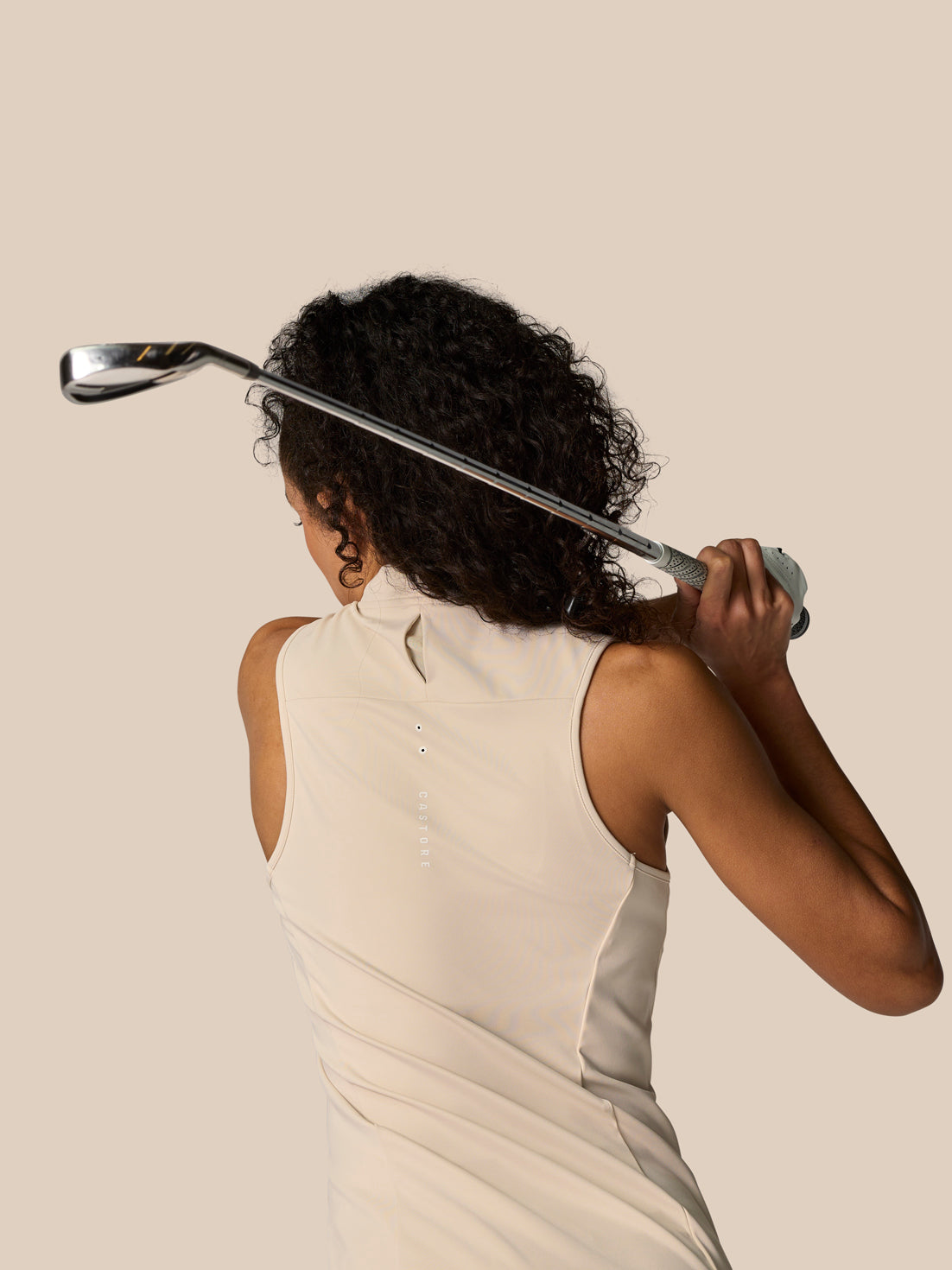 Back view of model in stone sleeveless top holding a golf club overhead, showcasing rear seam and smooth fabric