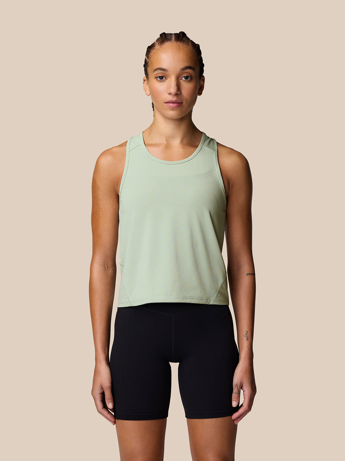 Woman wearing a sage Apex Training Tank Top with racerback silhouette against a beige backdrop