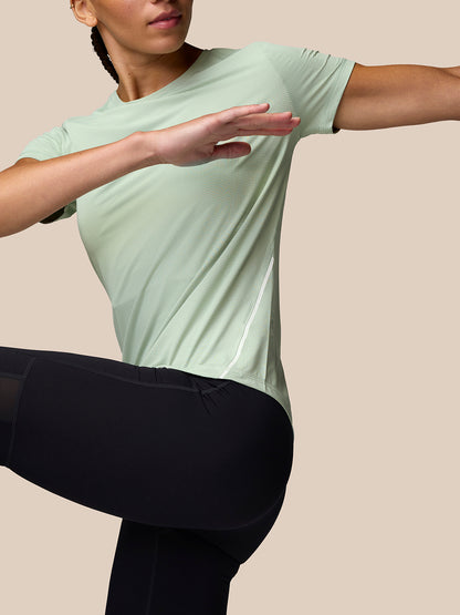 Model wearing Apex Training T Shirt Sage in sage green stretching, highlighting curved hem and side panel.