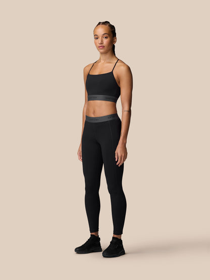 Model wearing Adapt Training Sports Bra in black with slim straps against a beige studio backdrop.