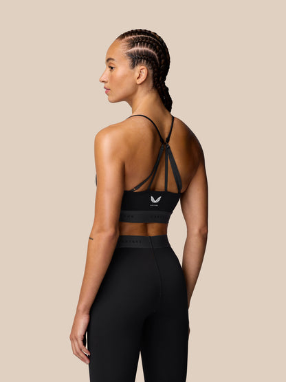 Back view of model wearing black Adapt Training Sports Bra with multi strap back and Castore logo band.