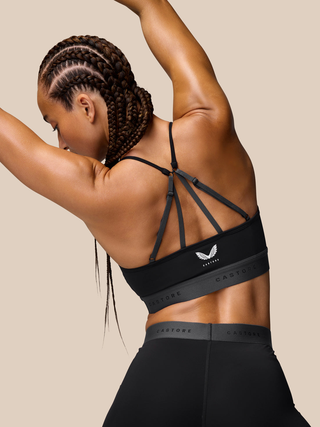 Back view of a model wearing the Adapt Training Sports Bra in black with crisscross thin straps and a Castore logo band.
