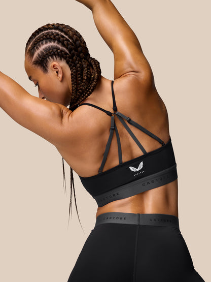 Back view of a model wearing the Adapt Training Sports Bra in black with crisscross thin straps and a Castore logo band.