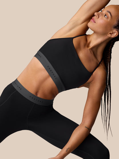 Side back shot of the Adapt Training Sports Bra in black showing an open back with multiple straps and Castore logo band.