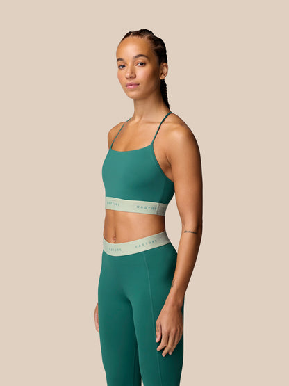 Model wearing seafoam Adapt Training Sports Bra with thin straps and matching leggings against a beige background.