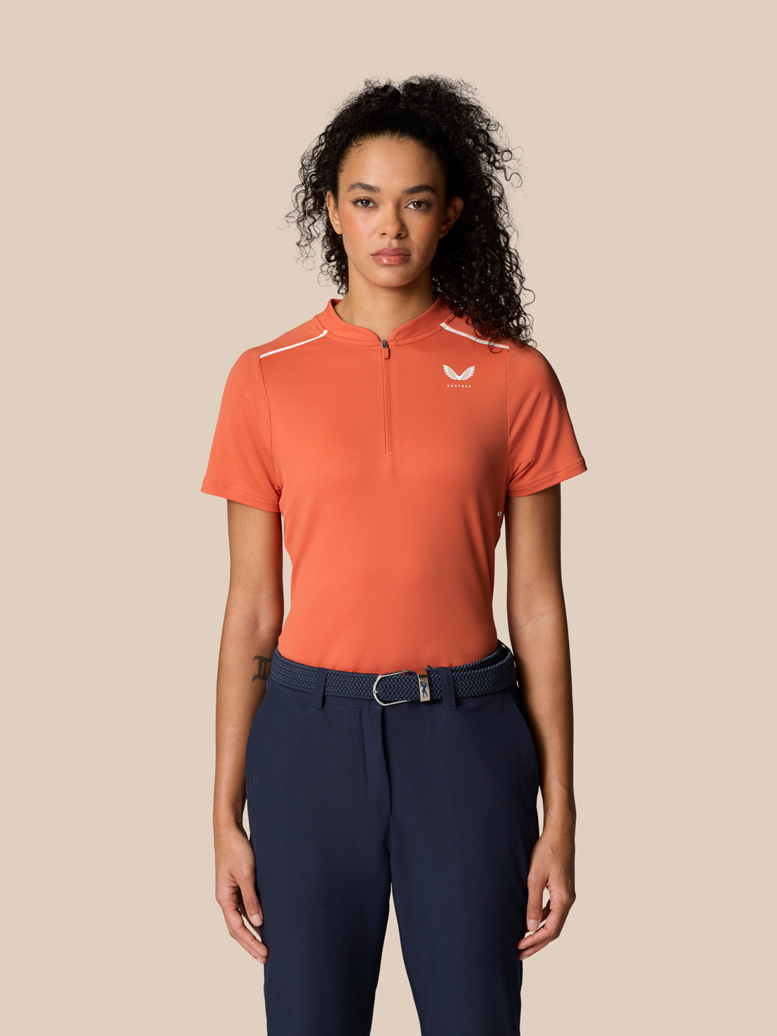 Woman in deep coral Pinnacle Polo with white piping and navy bottoms.