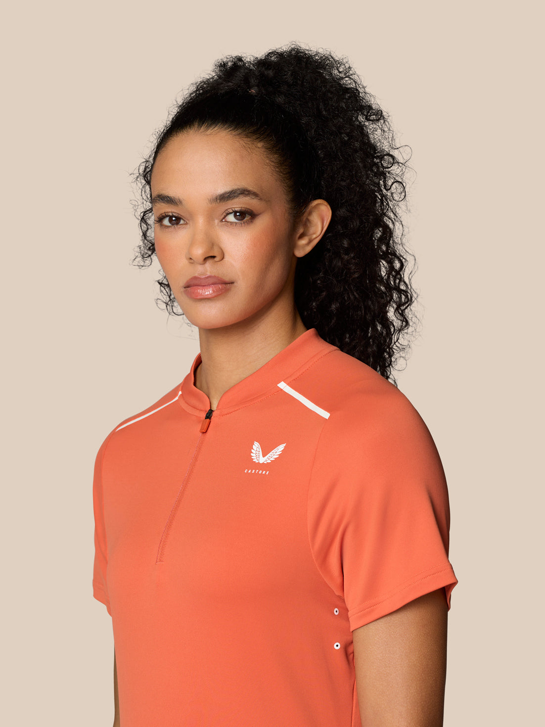 Front view of a model wearing Deep Coral Pinnacle Polo with a quarter zip and Castore logo on the left chest.