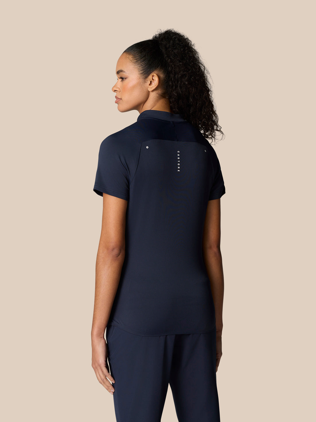 Rear view of a woman in navy Pinnacle Polo showing the back panel with Castore branding.