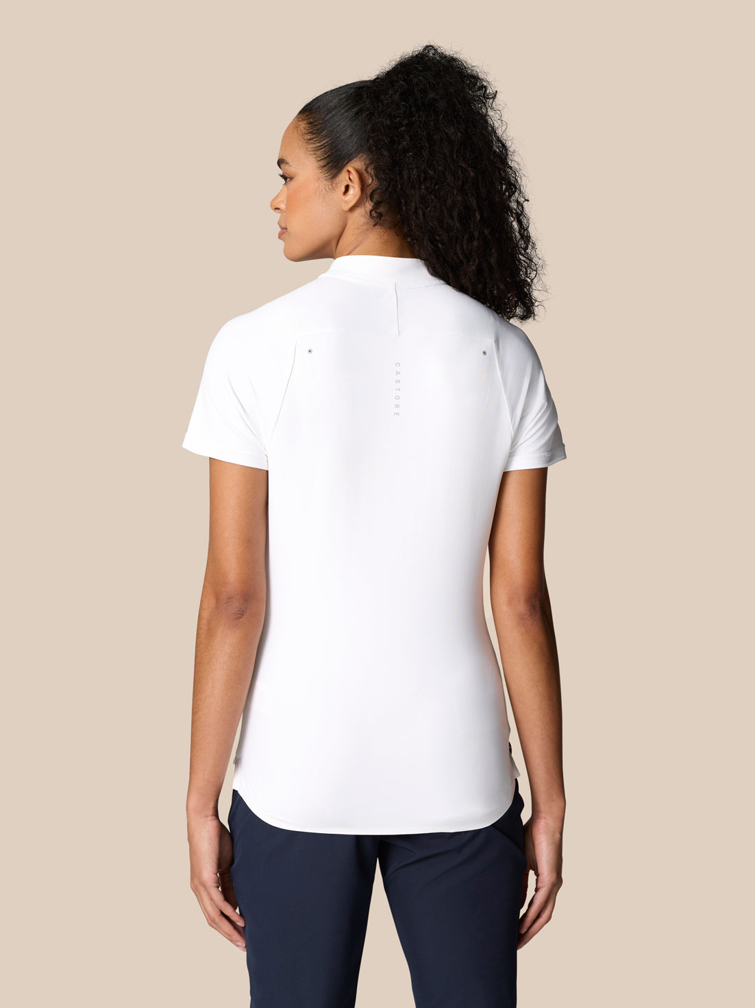 Back view of a woman in Pinnacle Polo White showing central branding along the spine