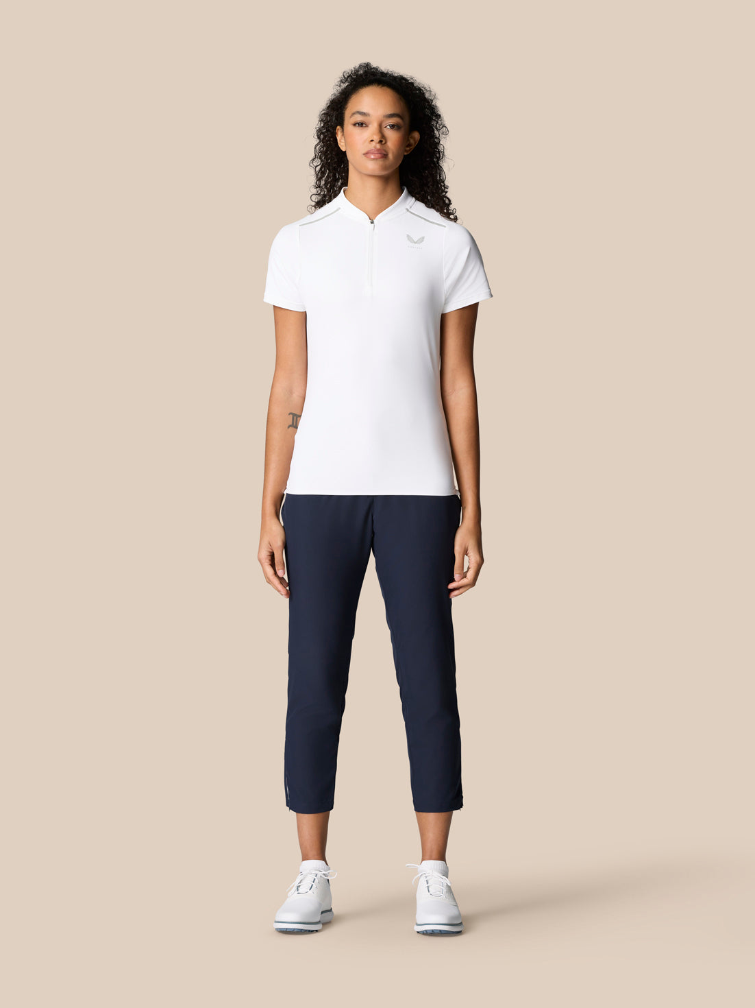 Front view of a woman wearing Pinnacle Polo White with navy pants, quarter zip and Castore logo on the chest