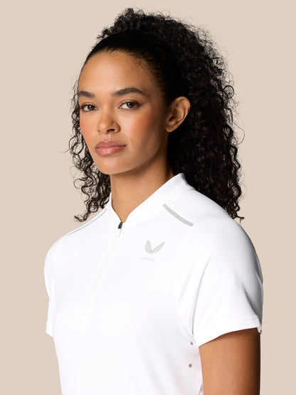Upper torso of woman in white Pinnacle Polo with zip placket and Castore crest on chest.