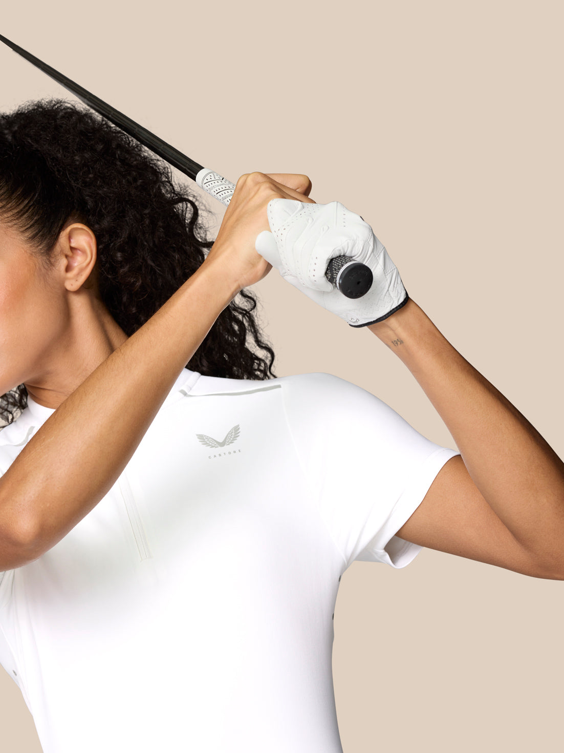 Female athlete wearing white Pinnacle Polo mid golf swing with a glove and Castore logo on the chest.