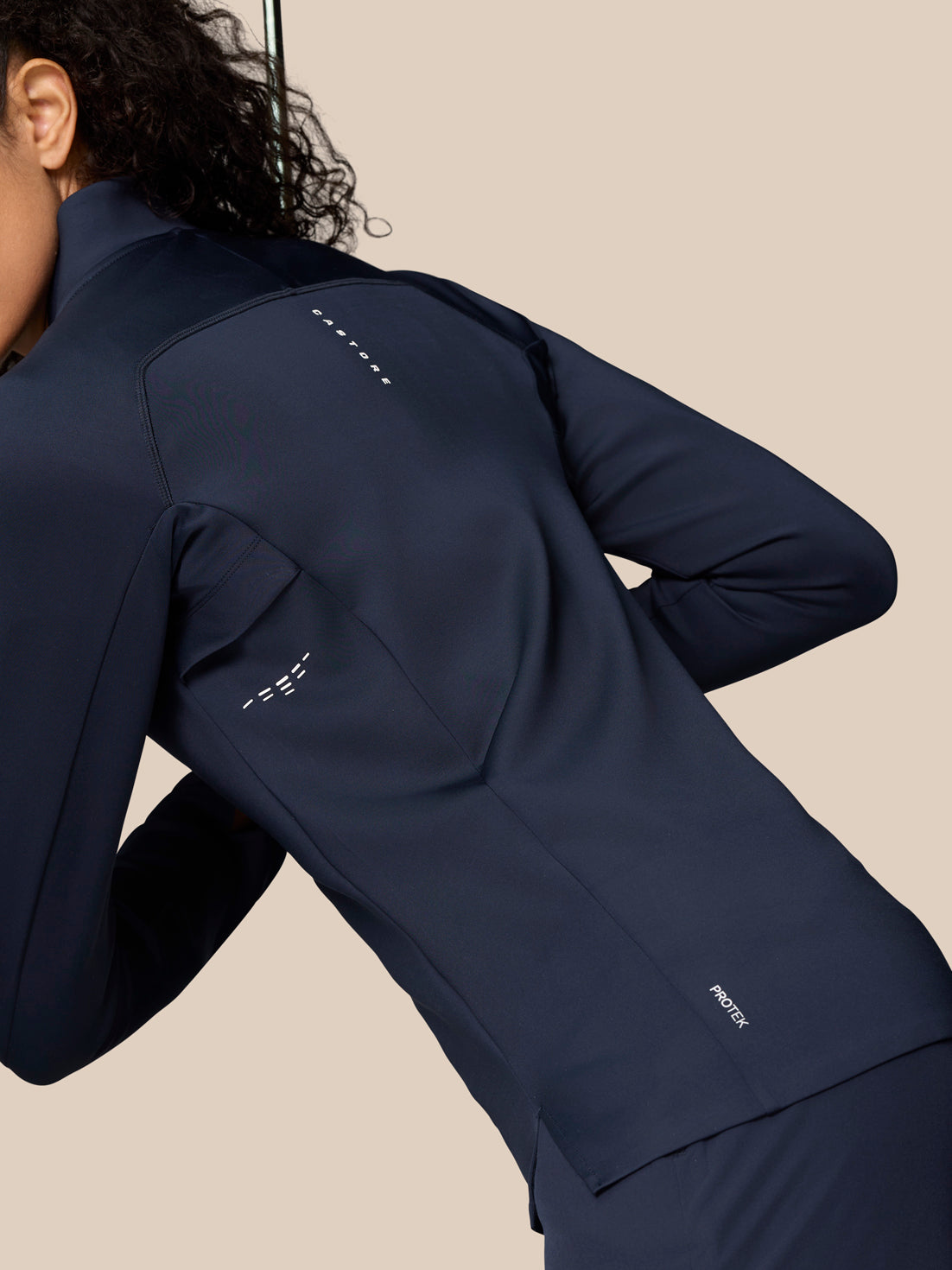 Angled back view of model wearing Midnight Navy Pinnacle LVS ½ Zip Top highlighting sleek silhouette and logo details.