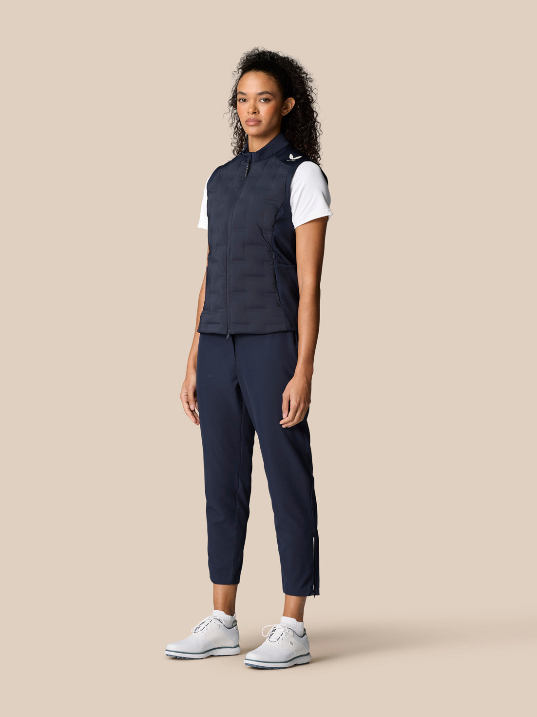 Full body shot of a woman in navy Pinnacle Hybrid Gilet with matching navy pants and white sneakers