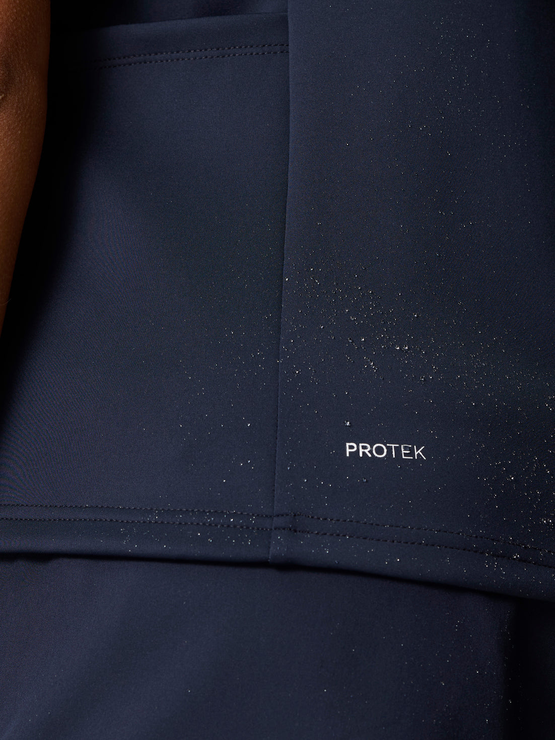 Close-up of navy Pinnacle Hybrid Gilet fabric showing PROTEK branding and scattered water droplets