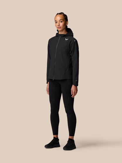 Full-body side view of a woman wearing the black Apex Training Wind Jacket with hood