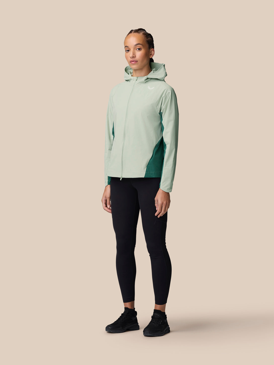 Full body view of model wearing Sage Apex Training Wind Jacket with hood and black leggings.