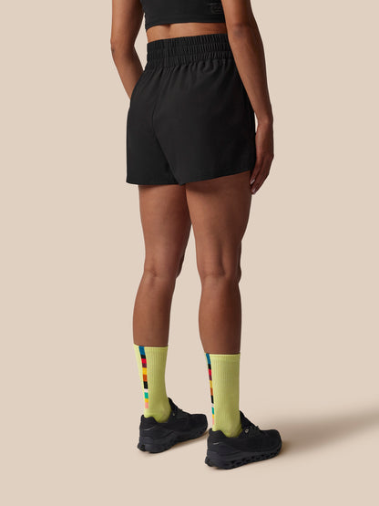 Person wearing black athletic shorts and yellow socks with a pattern on a beige background