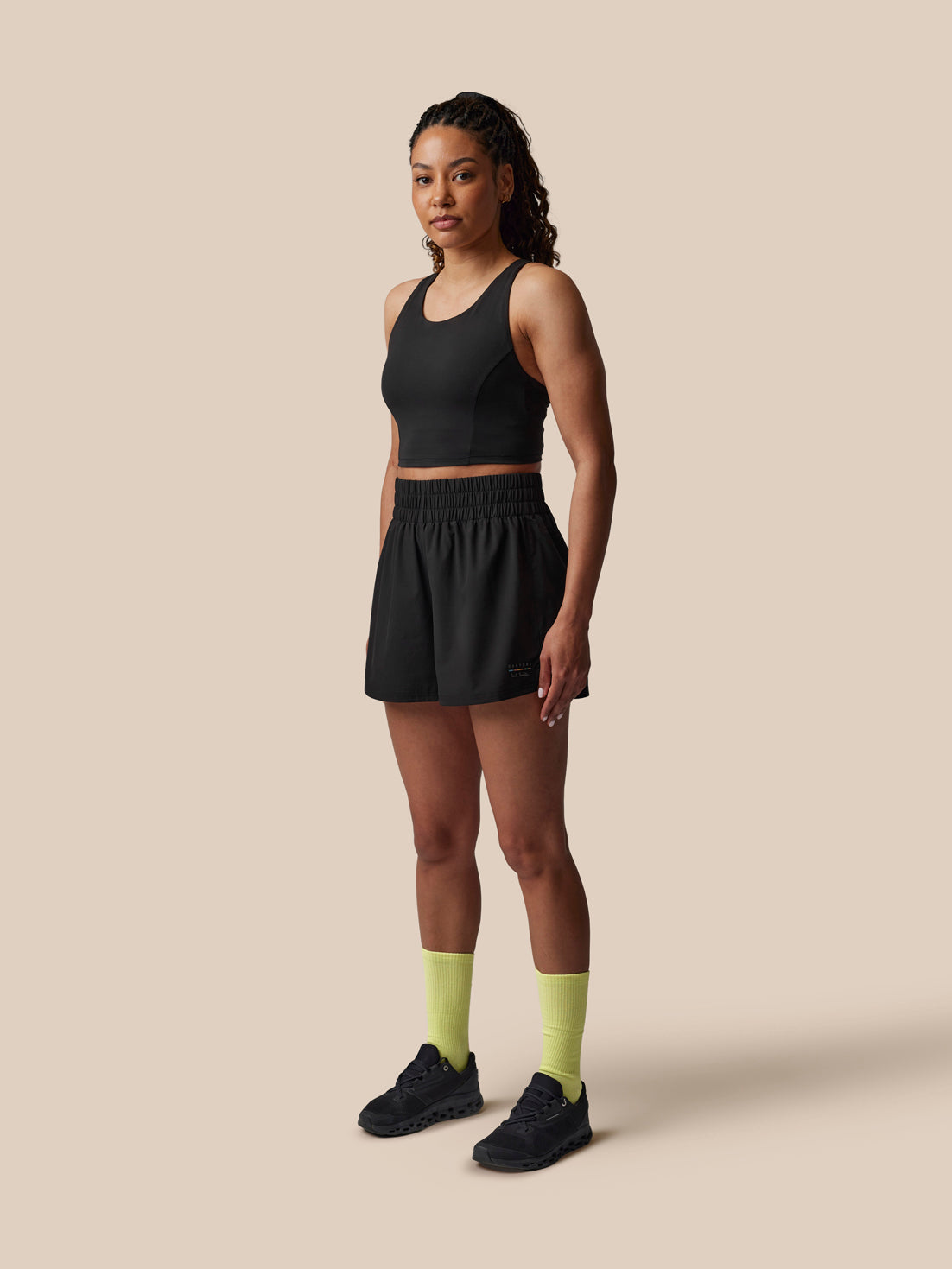 Woman wearing a black athletic outfit with yellow socks on a beige background