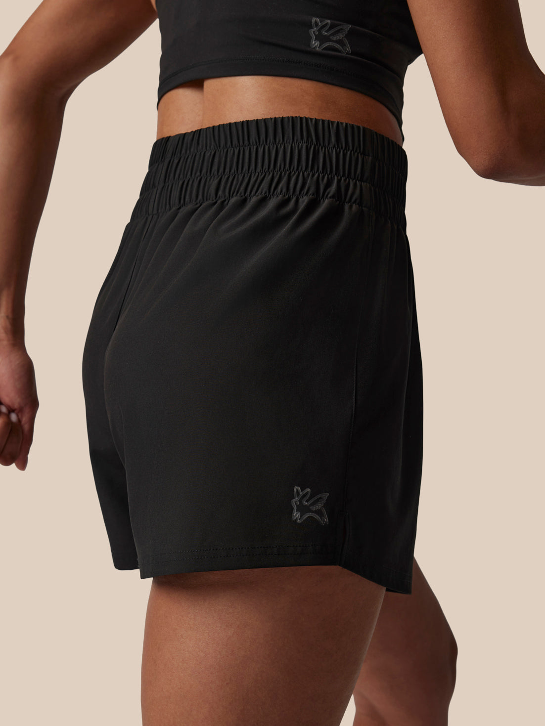 Person wearing black athletic shorts with a brand logo on a beige background