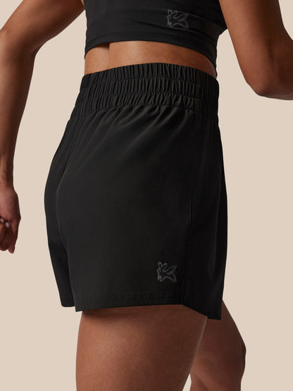 Person wearing black athletic shorts with a brand logo on a beige background