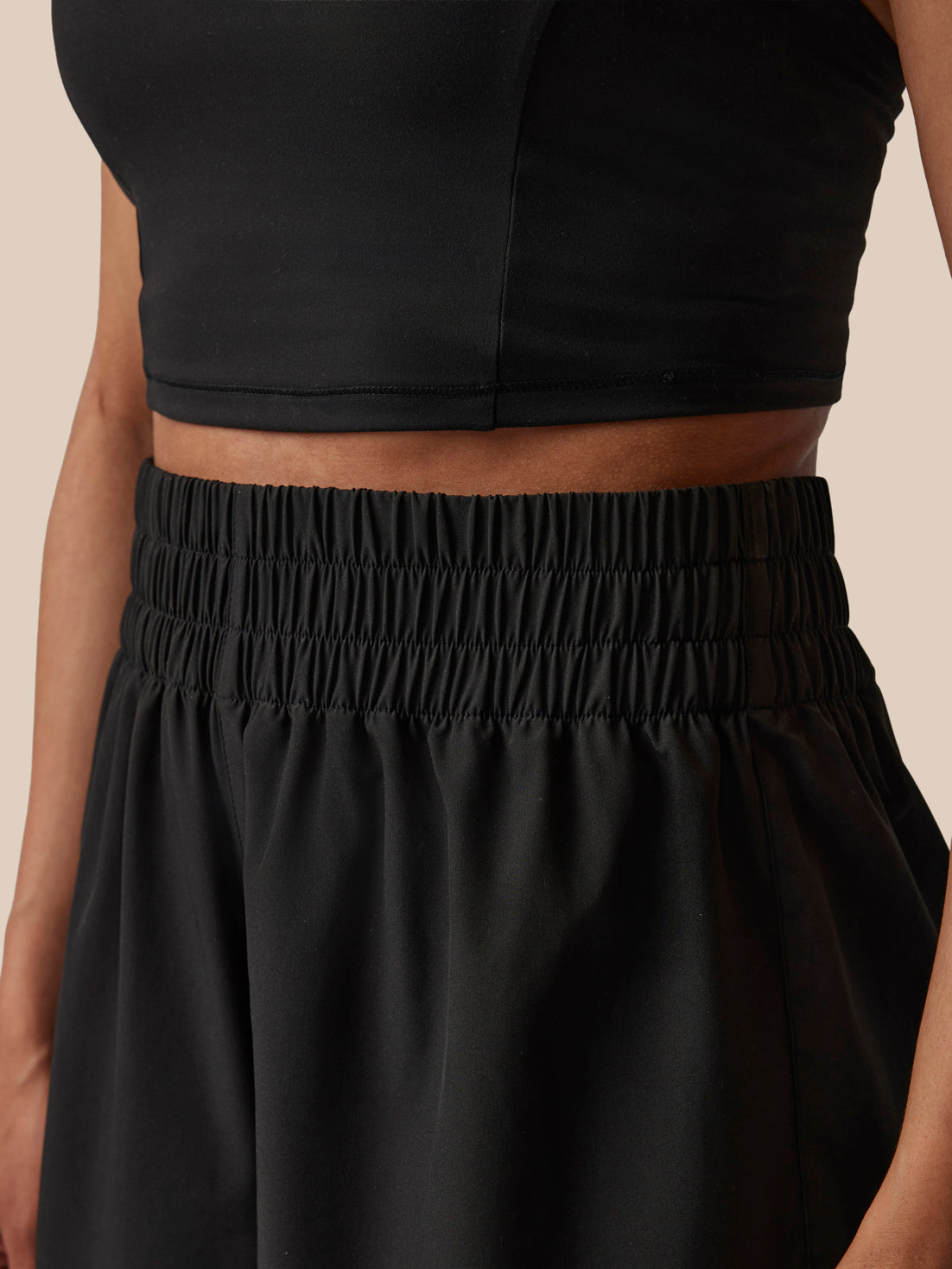 Person wearing a black crop top and black pants on a beige background