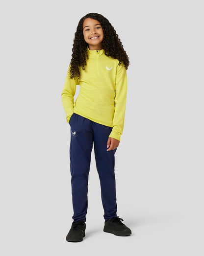 Full body view of a girl in a neon Citrus Junior Standard 1/4 Zip top with navy pants, hands in pockets.