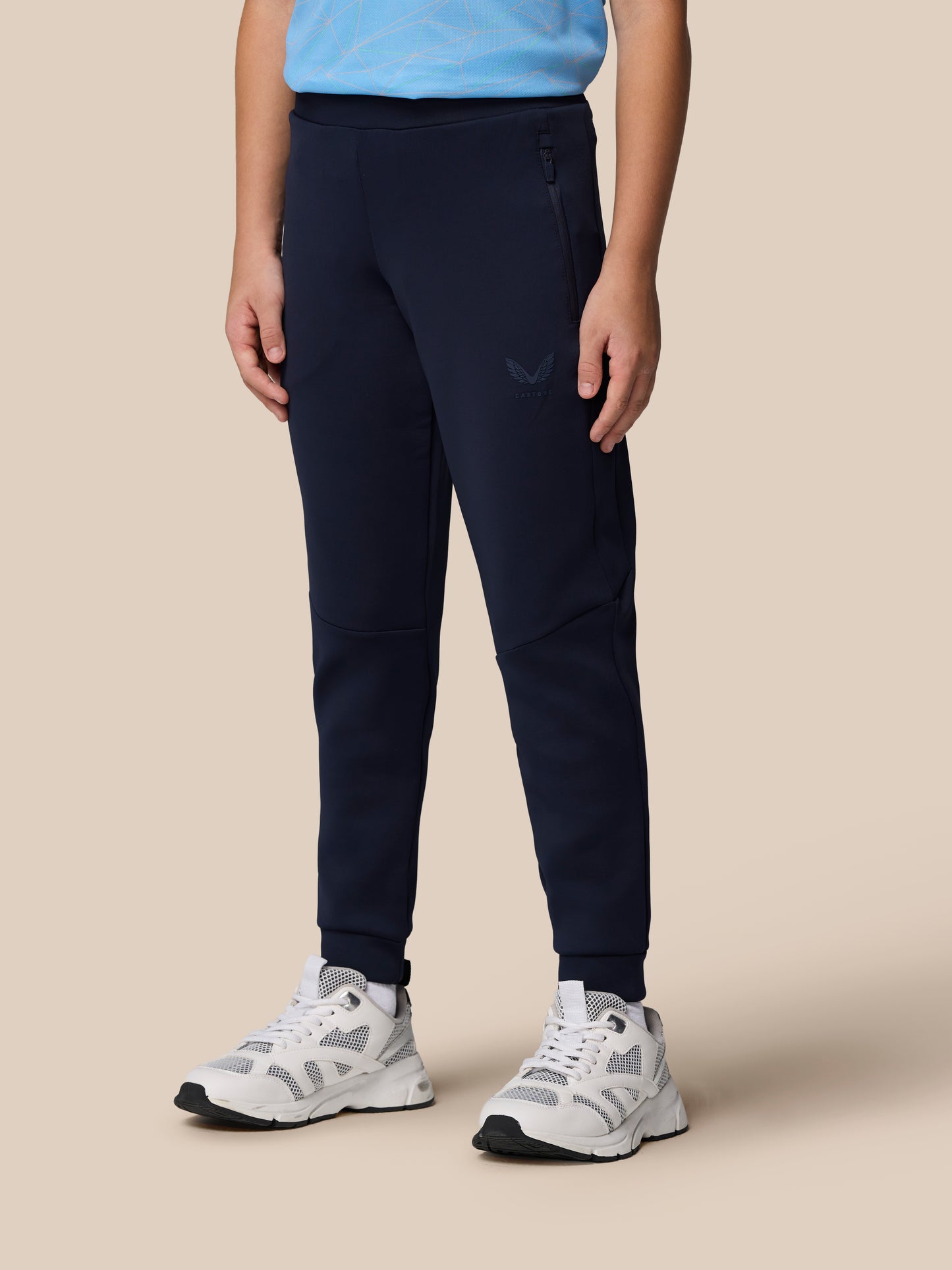 Close up of navy Junior Flex Scuba Trousers showing a zip pocket and Castore logo on the leg
