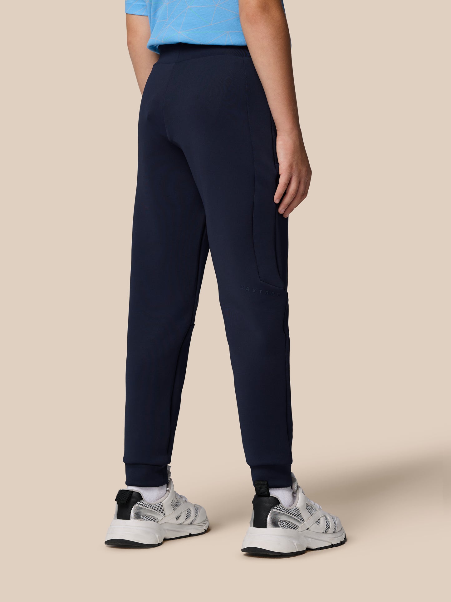 Back view of model wearing navy Junior’s Flex Scuba Trousers with zip pocket and Castore branding on the leg.