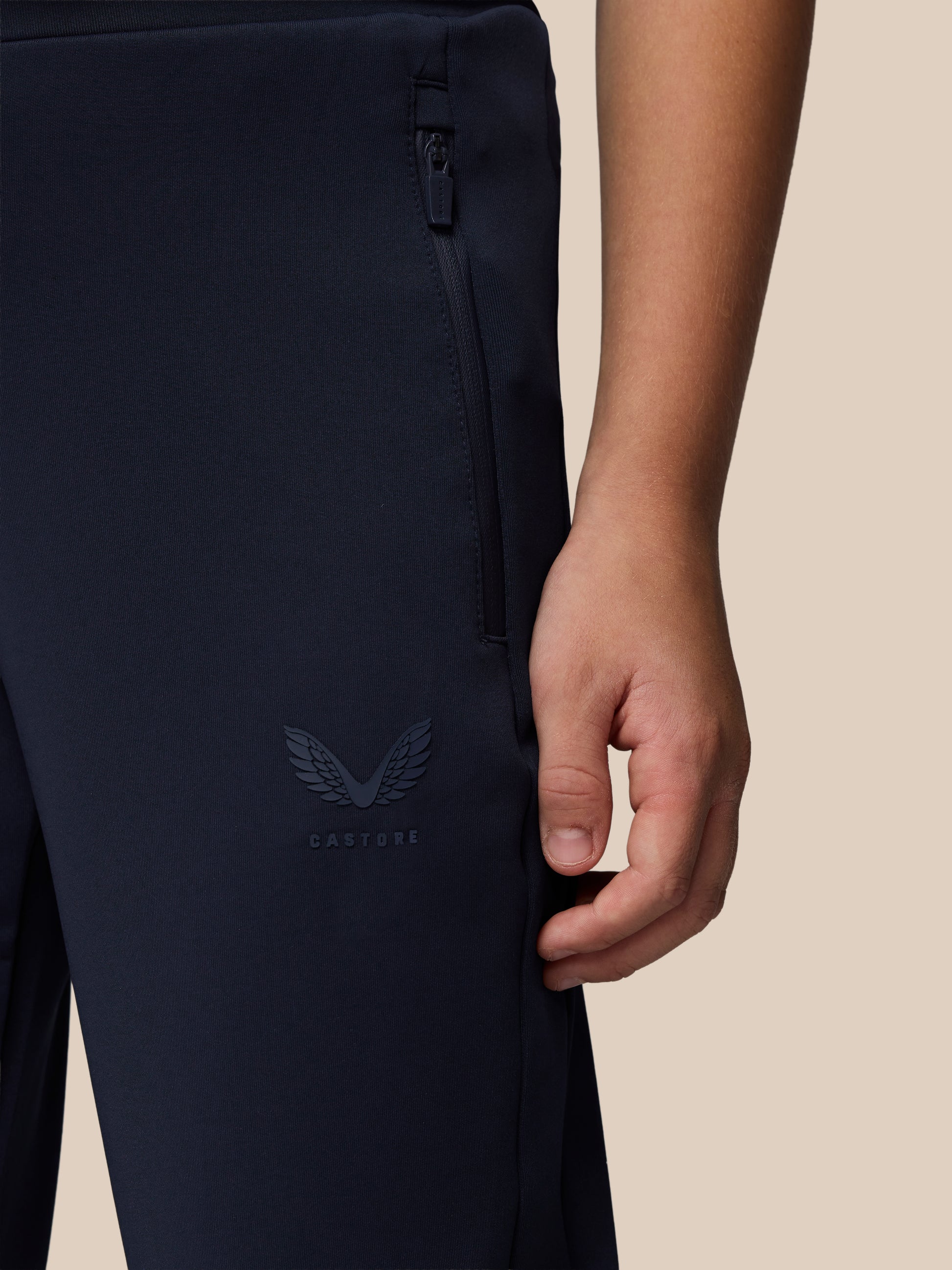 Close-up of navy Junior’s Flex Scuba Trousers showing a side zip pocket and Castore logo on the leg.