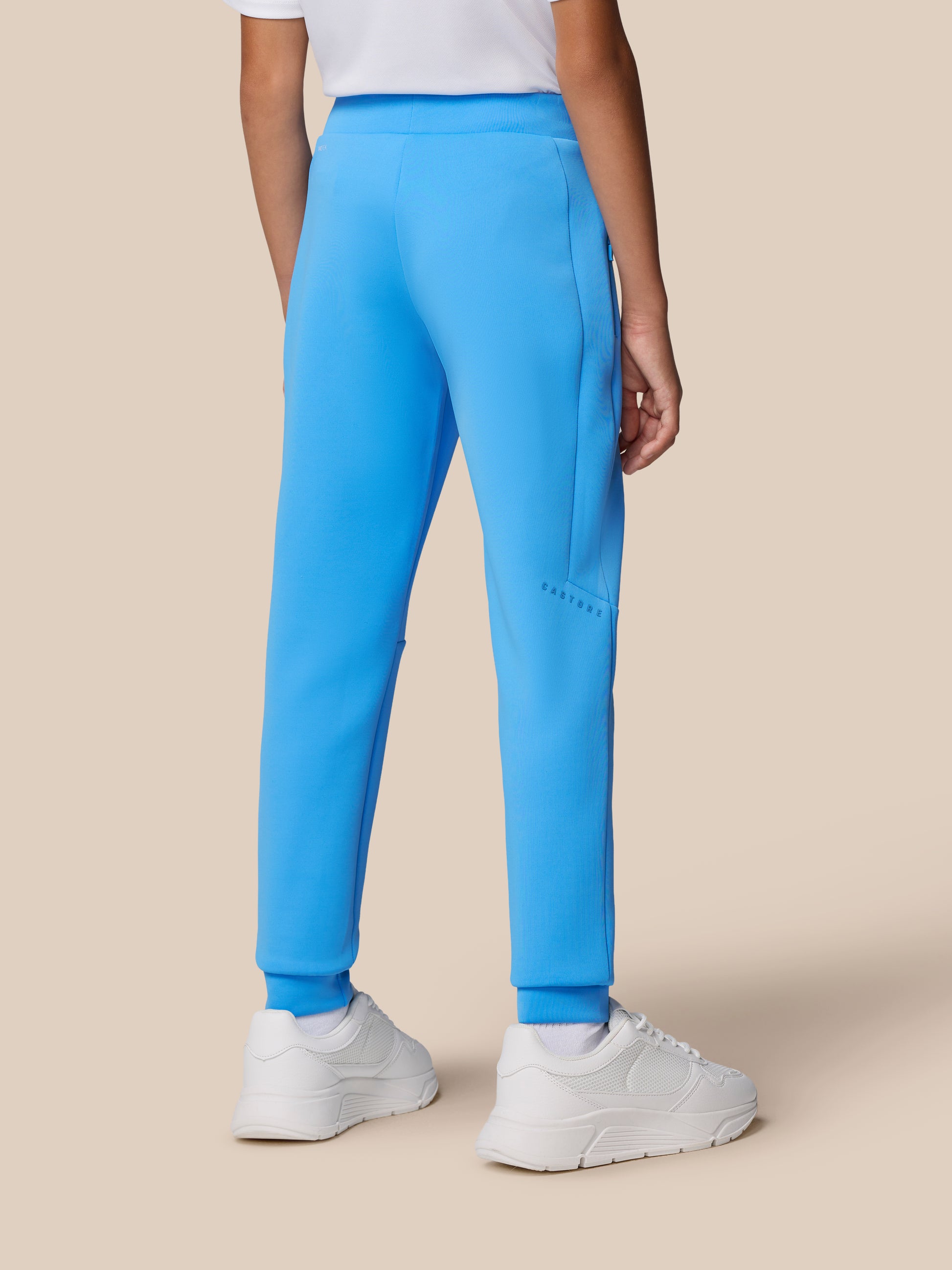 Lower view of blue Flex Scuba trousers showing the logo on the leg and side pocket with white sneakers