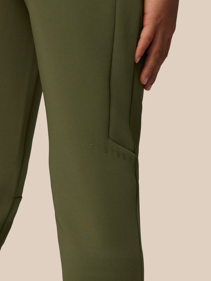 Close-up of olive green scuba fabric on a leg from Junior’s Flex Scuba Trousers, with a hand at the side and Castore branding embossed along the seam.