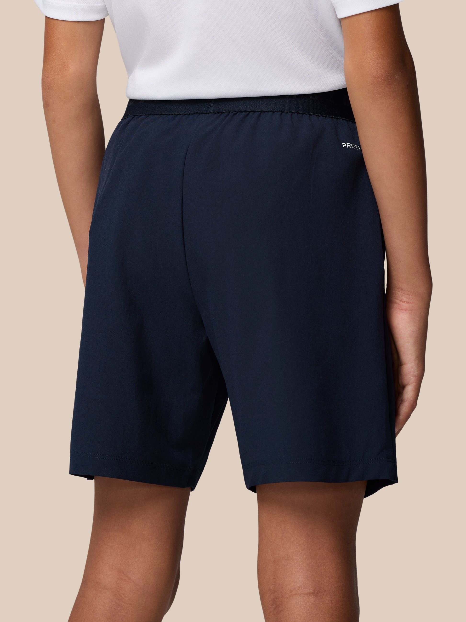 Rear view of navy Junior’s Adapt Woven Shorts featuring an elastic waistband and ProTek branding.