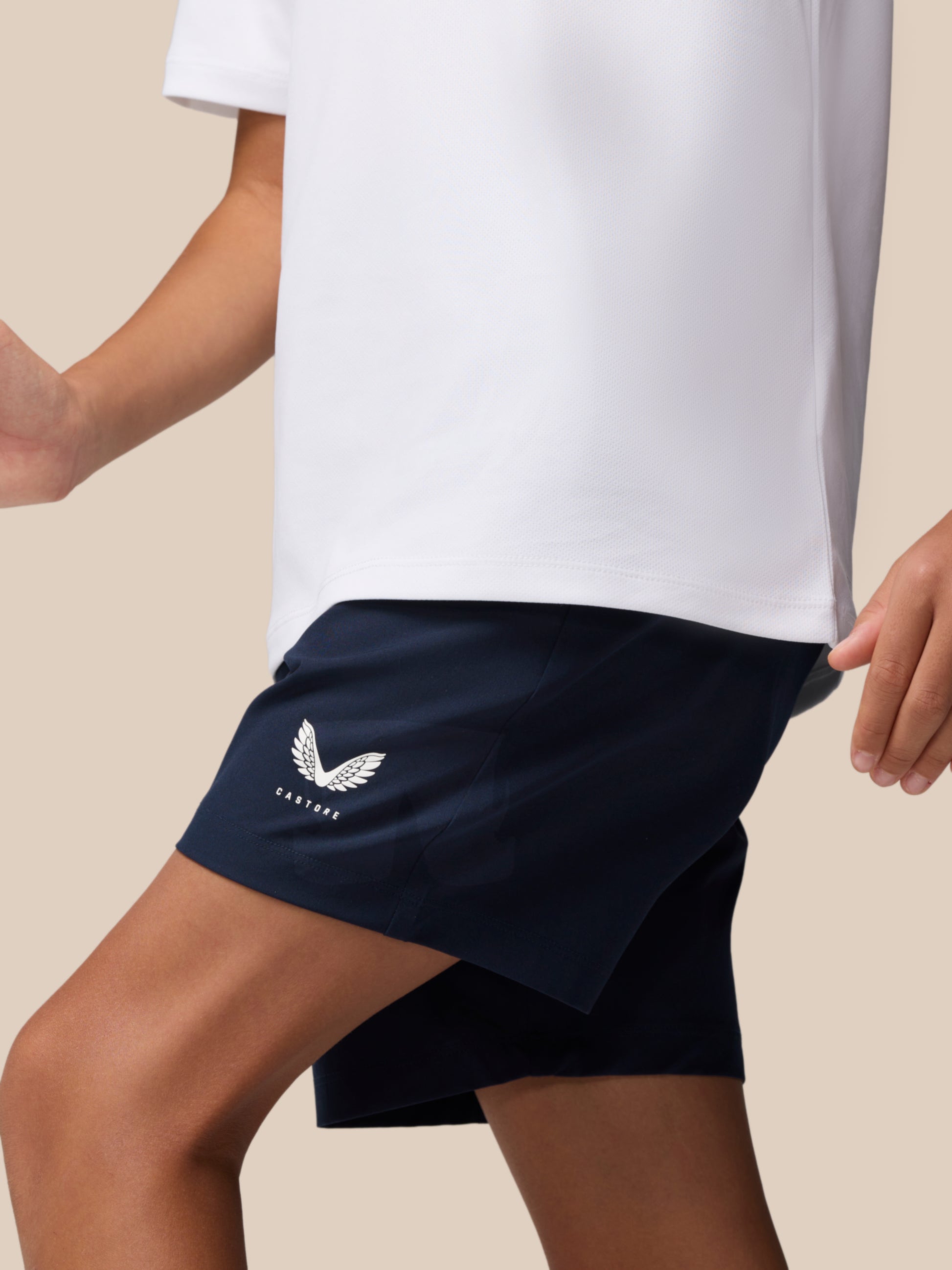 Side view of a young athlete wearing navy Adapt woven shorts with a white logo on the left thigh