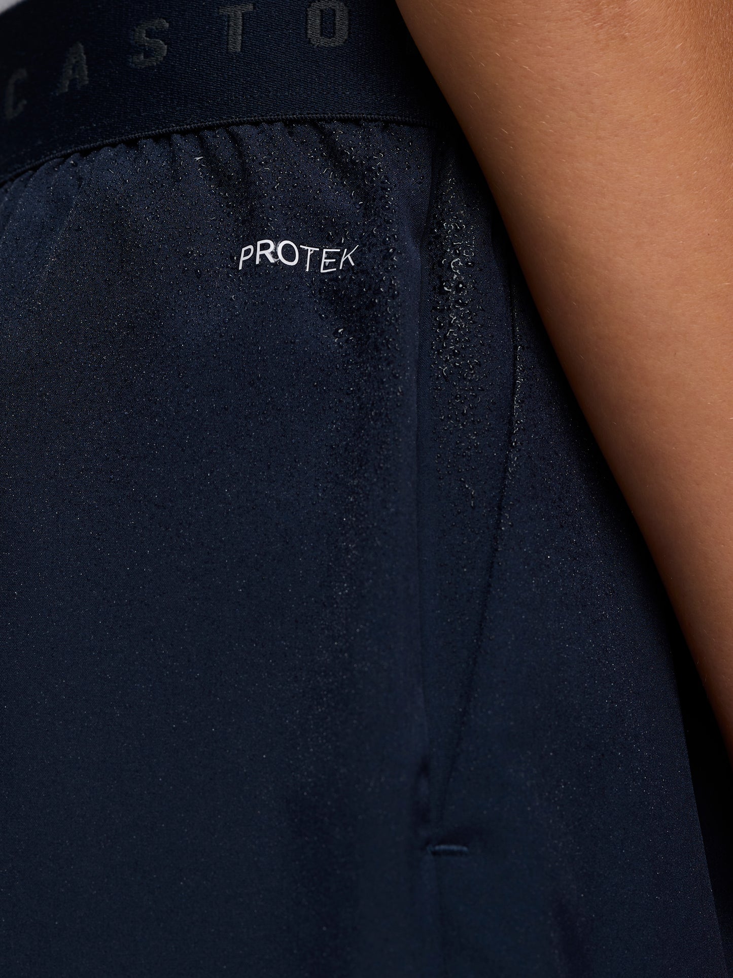 Close-up of navy Junior’s Adapt Woven Shorts fabric with water droplets and ProTek branding