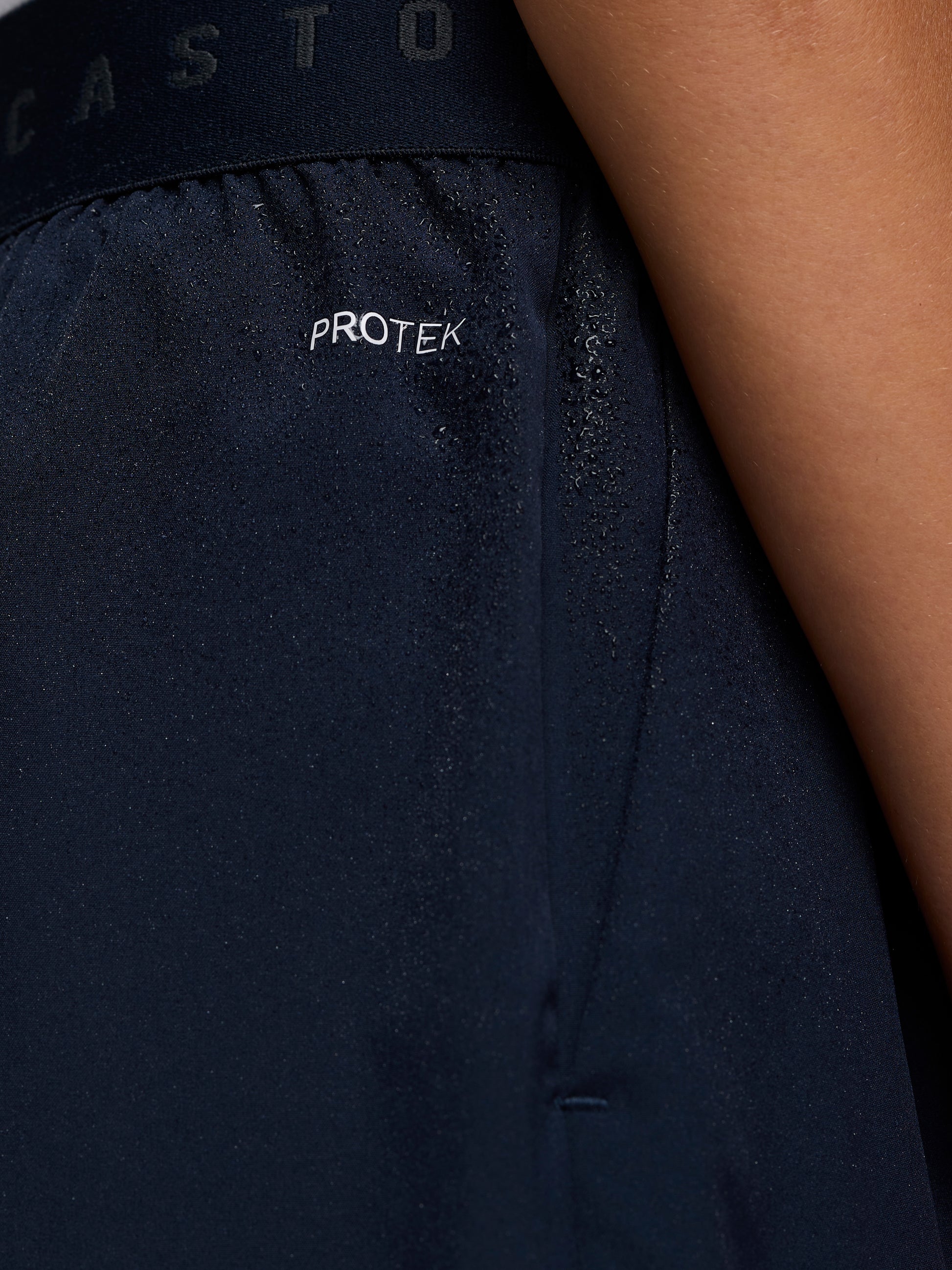 Close-up of navy Junior’s Adapt Woven Shorts fabric with water droplets and ProTek branding