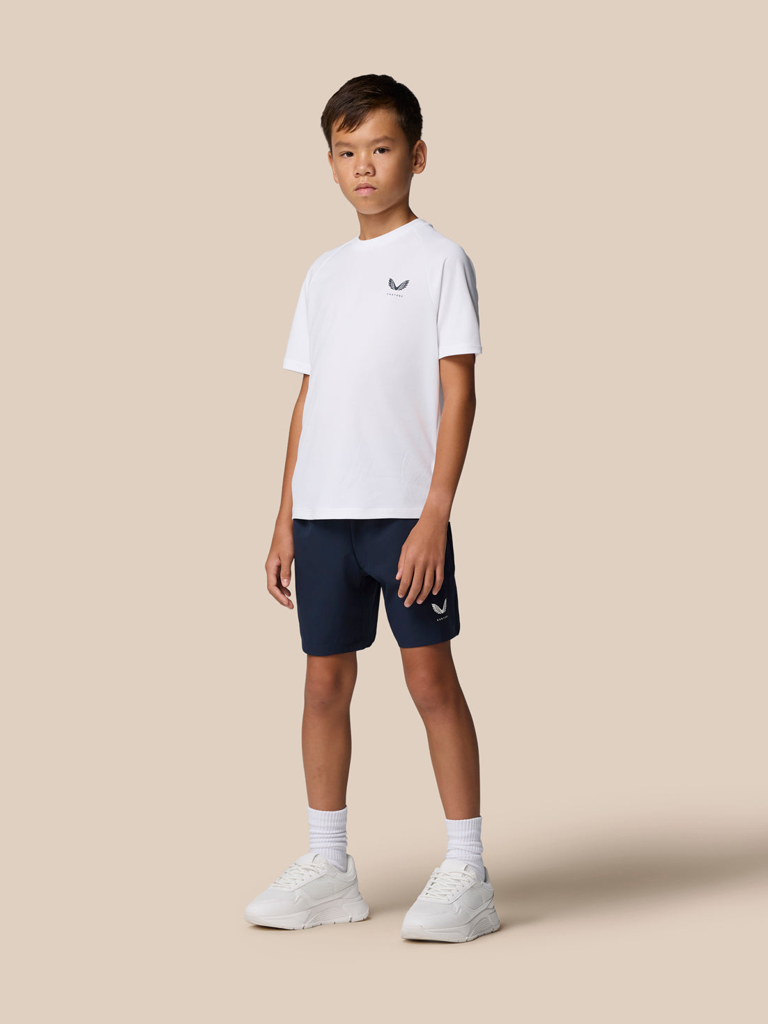 Side view of a boy in a white Junior's Adapt Training T-Shirt with Castore logo on the chest and navy shorts