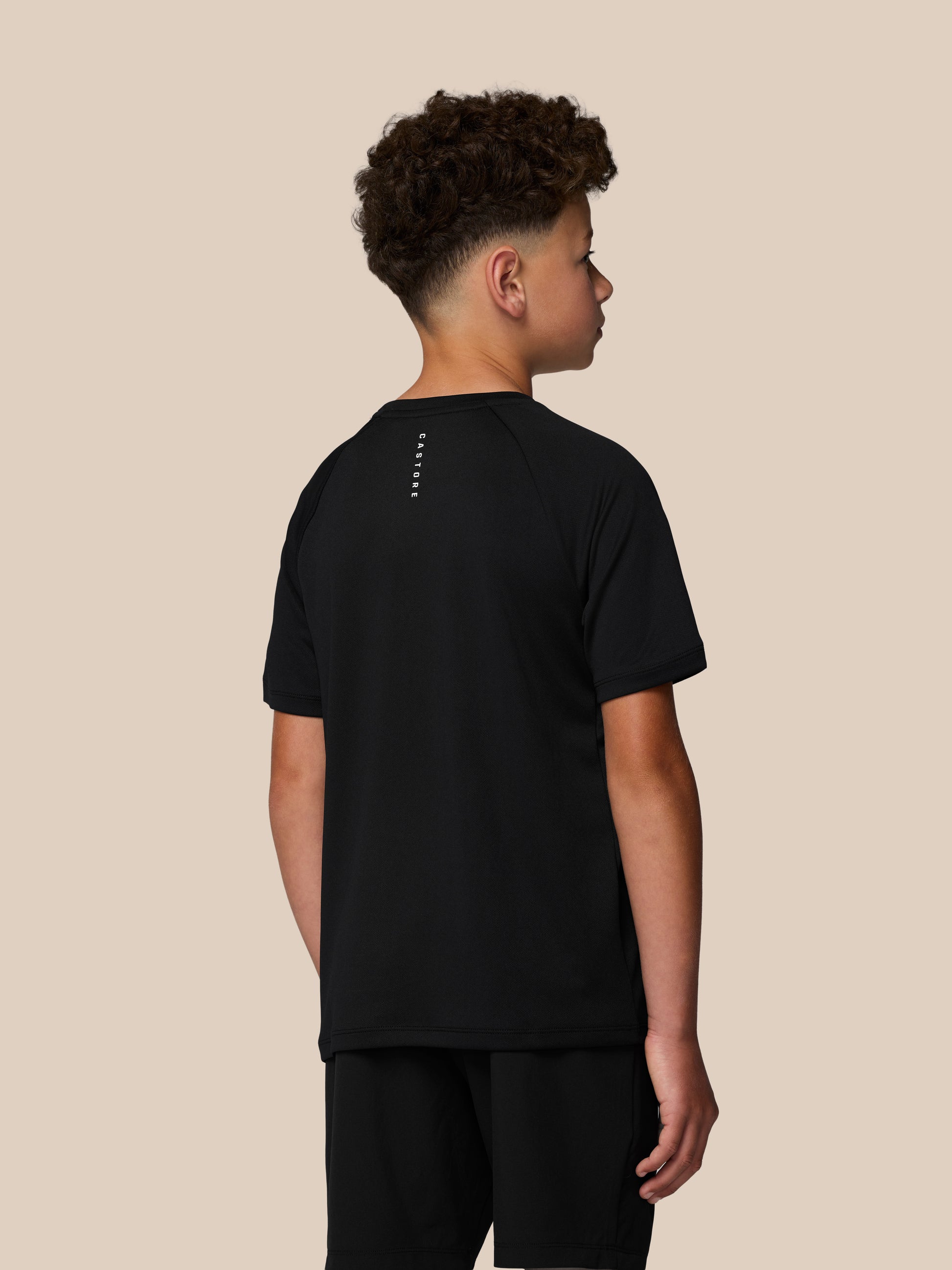 Rear angled view of a boy in black Castore Adapt T Shirt with vertical CASTORE text along the back.