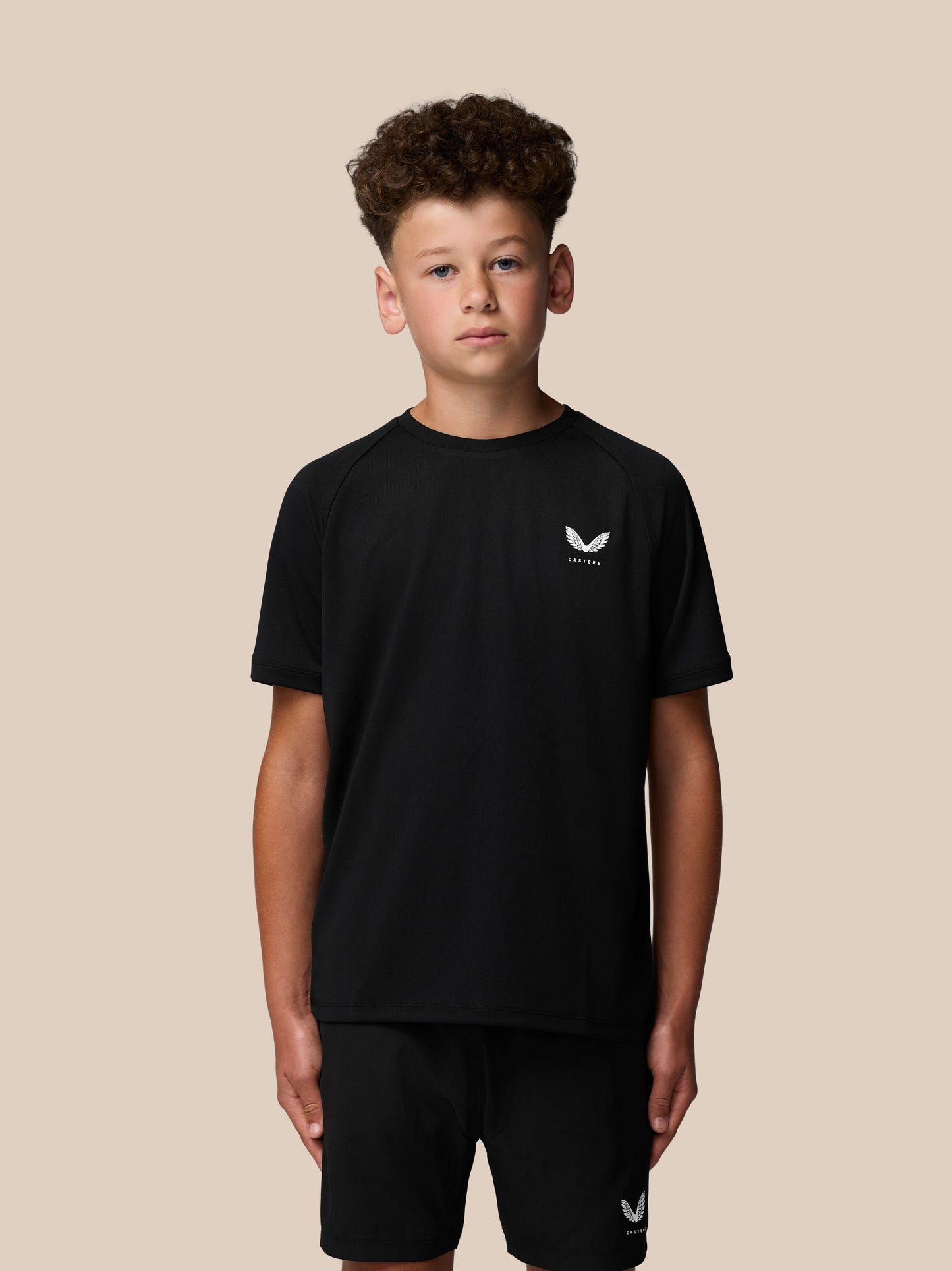 Back view of a young boy in a black Castore Adapt T Shirt showing vertical CASTORE text on the upper back.
