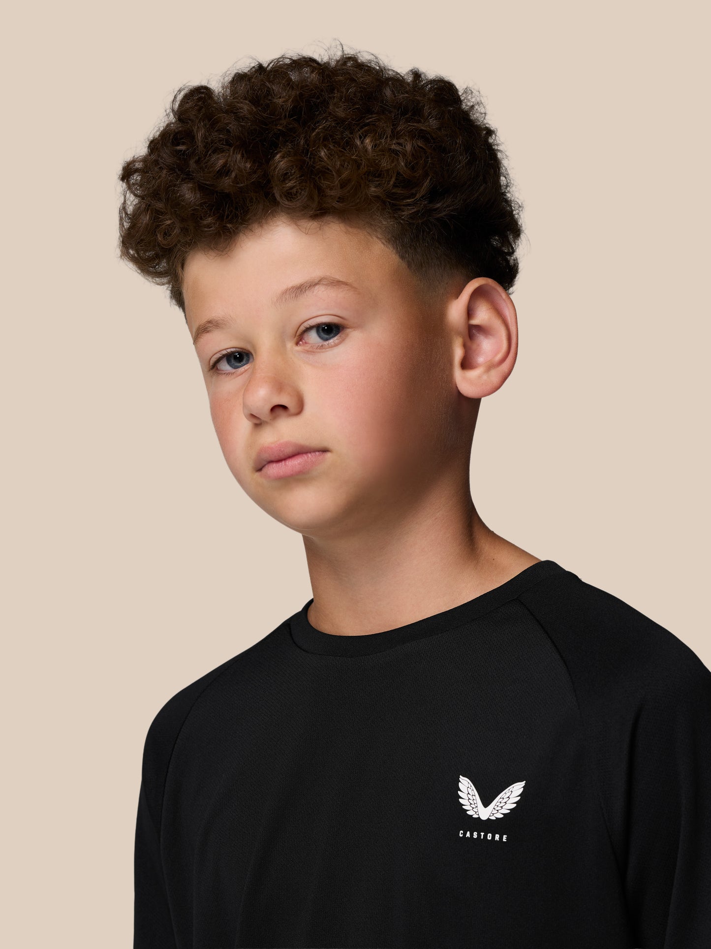 Portrait of a boy in a black Castore Adapt Short Sleeve T Shirt with a white logo on the chest