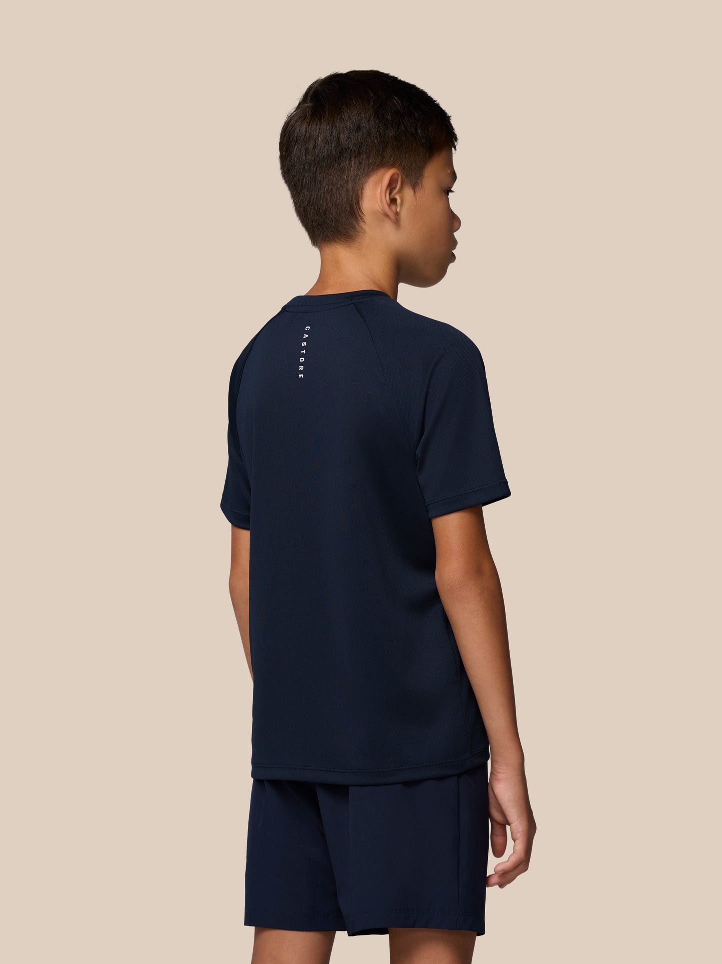 Rear view of a young boy in navy Castore Adapt Short Sleeve T Shirt with branding along the back.
