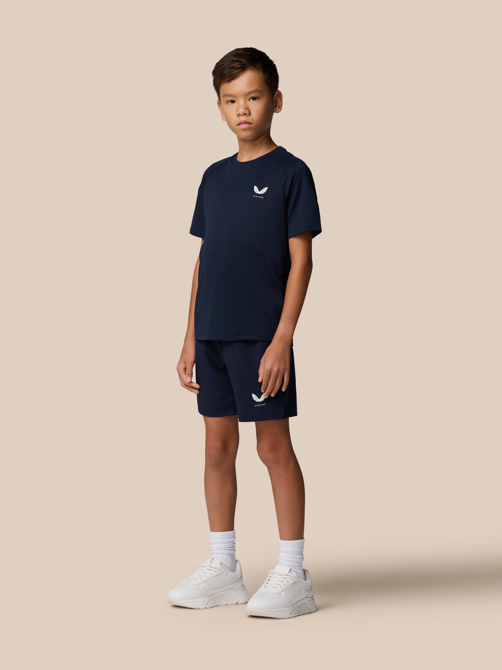 Front view of a boy in navy Adapt Short Sleeve T Shirt and shorts with Castore logos on the left chest and leg.