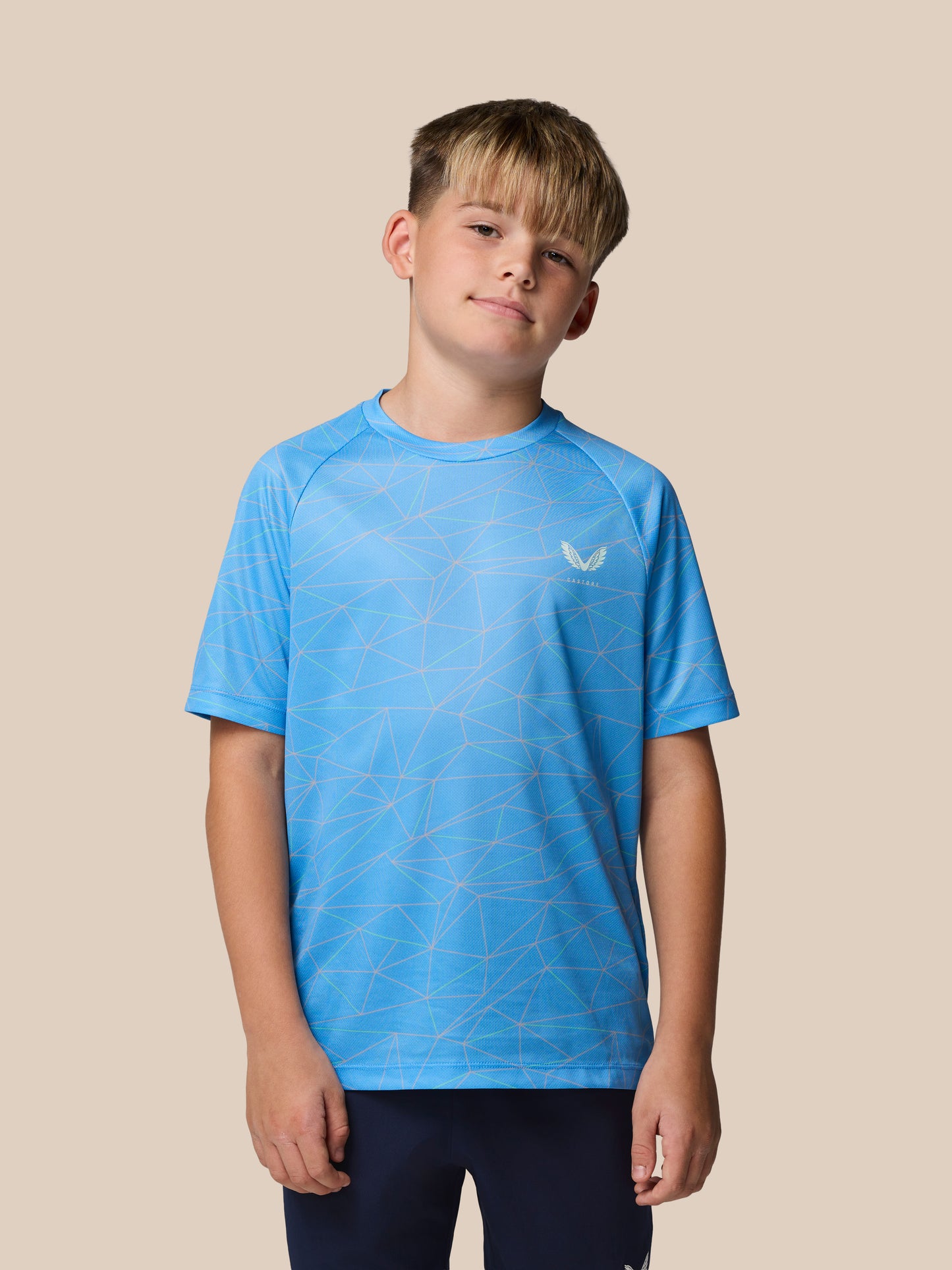 Boy wearing a blue geometric print short sleeve T shirt with Castore logo on the chest